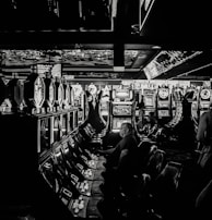 A dimly lit casino filled with rows of slot machines, some occupied by people. The machines' lights contrast with the dark surroundings, creating a vibrant yet subdued atmosphere.