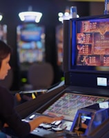 A person is seated at a slot machine console in a casino, focusing intently on the game displayed on the screen. The background shows several other illuminated gaming machines, adding a vibrant and colorful atmosphere to the scene.