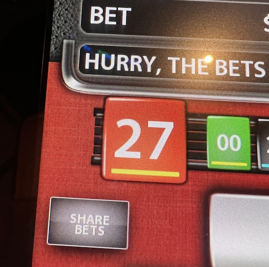 A digital display screen showing a casino betting interface, with text prompting to hurry bets and a highlighted number 27 in red. There are options for betting amounts and a 'share bets' button.